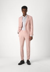 Completo rosa chiaro con design slim fit, giacca a un bottone e pantaloni abbinati. Presenta una camicia bianca sotto e scarpe eleganti nere.
