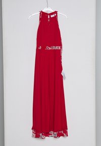 Robe maxi rouge sans manches avec bordure fleurie à la taille, à l'encolure et à l'ourlet, suspendue sur un cintre transparent contre un mur blanc.