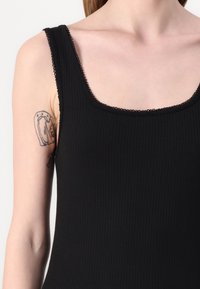 Musta ribbitetty tank top, jossa on neliön muotoinen kaula-aukko, koristeellista ommeltua reunaa ja tiukka siluetti.