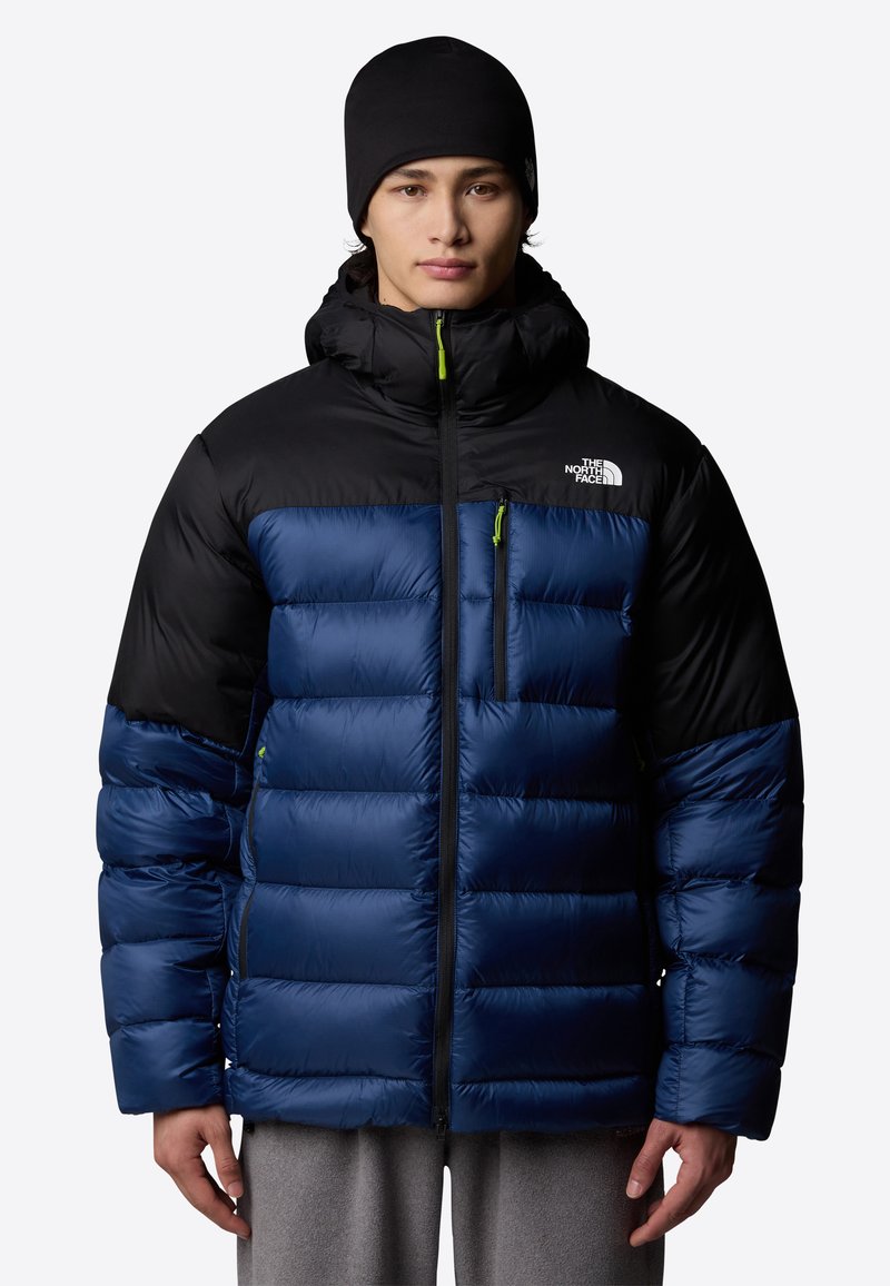 Niebieska i czarna kurtka puchowa z kapturem, z kwadratowymi przeszyciami, z przodu zapinana na zamek oraz z kieszenią na piersi. Odbijające światło logo na klatce piersiowej.