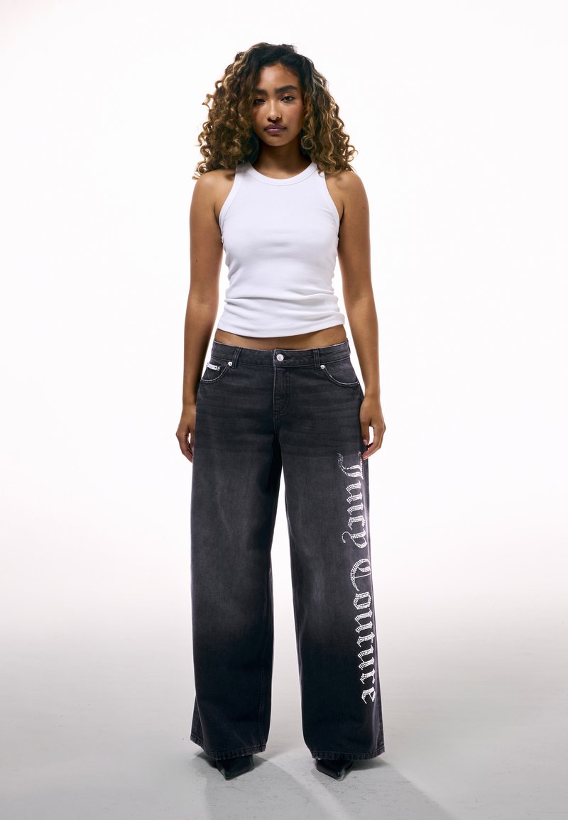 Τζιν παντελόνι με φαρδιά γραμμή σε σκούρο γκρι χρώμα με ασημί λεπτομέρειες στο πλάι, συνδυασμένο με εφαρμοστό λευκό τοπ χωρίς μανίκια. Διαθέτει τσέπες μπροστά και κλείσιμο με κουμπιά.