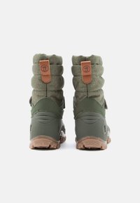 Zöld túrázó cipők struktúrált textil felsőrésszel, párnázott bokarésszel, és strapabíró gumitalppal, amelyen barázdált minta található, bőr díszítéssel kiegészítve.
