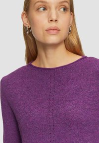 Pull en maille violet avec un col rond, tissu texturé et détail de couture verticale sur le devant. Fini lisse et épaisseur moyenne.