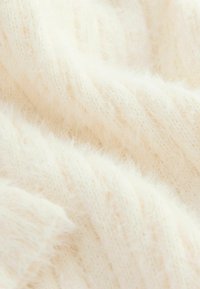 Tissu tricoté de couleur crème avec une texture douce et pelucheuse, présentant un motif côtelé, avec des lignes horizontales subtiles.
