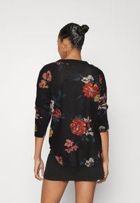 Svart stickad topp med färgglada blommönster, trekvartslånga ärmar, rundad nederkant och ribbad halsringning.