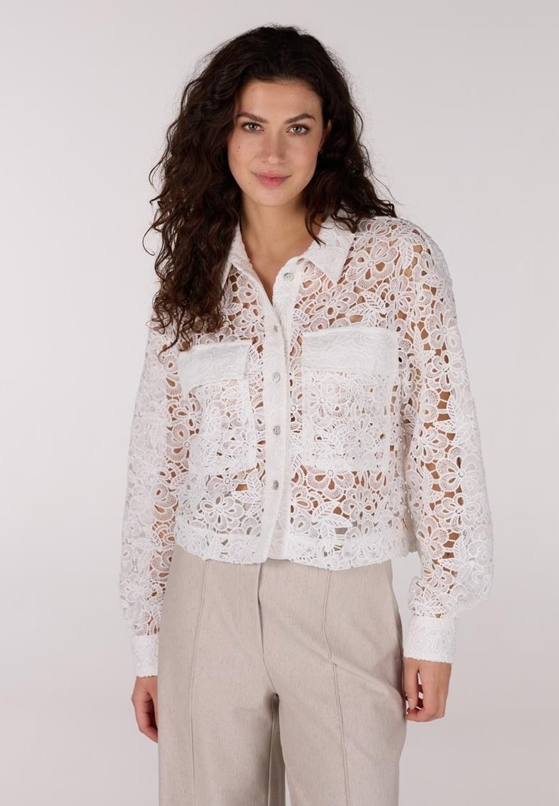 Witte kanten crop-top met bloemenpatroon, knopen aan de voorkant en twee borstzakken; heeft lange mouwen met manchetten.