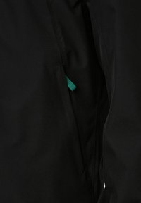 Tessuto nero con una texture liscia, dotato di una tasca laterale con spacco e un passante in tessuto verde per un facile accesso.