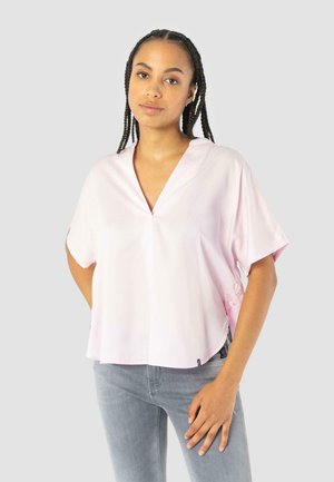 Blusa rosa chiaro a maniche corte con scollatura a V e dettagli laterali con bottoni. Realizzata in un tessuto morbido. Abbinata a jeans grigi chiari slim-fit.