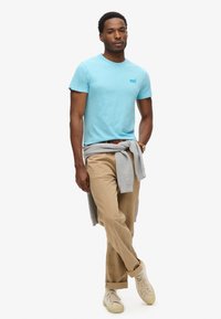 T-shirt azzurro chiaro a maniche corte con scollo a girocollo, pantaloni khaki, maglione grigio legato in vita e sneakers beige.