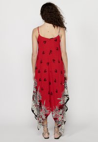 Robe rouge avec des motifs de feuilles noires, fines bretelles et un ourlet superposé avec des accents floraux blancs. Tissu léger et fluide.