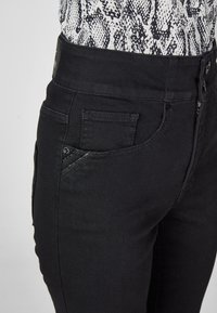 Black denim jeans with a high waist, featuring a side pocket, subtle stitching details, and a smooth texture.