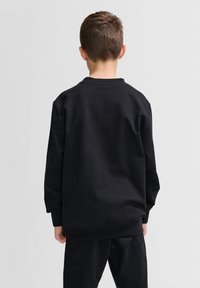 Felpa nera con maniche lunghe e collo rotondo. Tessuto liscio e vestibilità comoda. Pantaloni neri coordinati visibili in basso.
