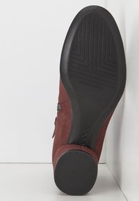 Bota de tobillo de ante marrón con un acabado suave, cremallera lateral y una suela de goma negra texturizada con un patrón geométrico.
