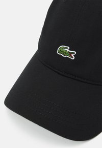 Fekete baseball sapka ívelt széllel és hímzett zöld krokodil logóval. Texturált anyaggal és látható varrás részletekkel rendelkezik.