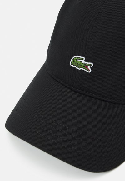 Casquette de baseball noire avec une visière courbée et un logo de crocodile vert brodé. Présente un tissu texturé et des accents de couture visibles.