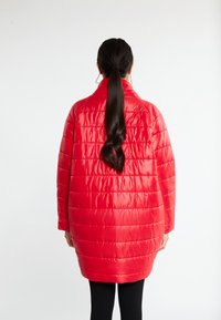 Rød polstret frakke med høj krave, der har en horisontal quiltet design og sidelommer, lavet af et skinnende, glat stof.
