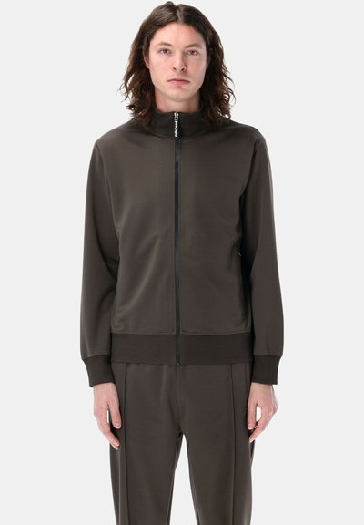 Giacca da tuta marrone scuro con colletto alzato, zip frontale completa e polsini a coste, realizzata in tessuto liscio ed elastico.