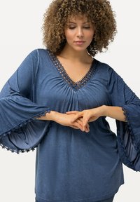 Top leggero blu con scollatura a V e dettagli in pizzo floreale lungo il collo e maniche a campana. Tessuto morbido con una vestibilità comoda.