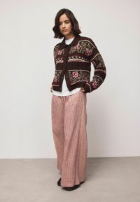 Cardigan maro cu model floral și accente roz, purtat peste o cămașă albă și asortat cu pantaloni largi roz cu carouri. Textură netedă.