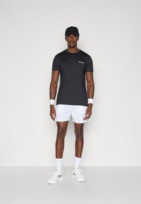 Juoda trumpa sportinė marškinė su pilku logotipu; baltos sportinės šortai; baltos kojinės; baltos sportbačiai; juodas kepurė su įspaustu tekstu.