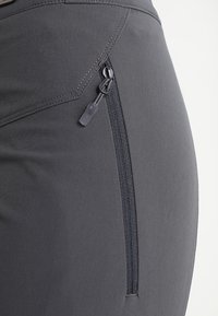 Grijze sportlegging met zijzak met rits, gladde textuur en contrasterende stiksels langs de naad, die het strakke ontwerp benadrukken.