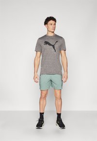 Gray athletic t-shirt with a black Puma logo, paired with mint green shorts. Model wears black sneakers with green accents and black socks.