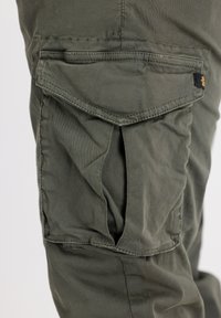 Pantalones cargo en verde oliva con un bolsillo lateral con tapa, hechos de una tela suave y texturizada con detalles de costura visibles.