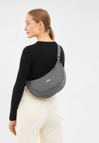 Borsa a tracolla grigia con un design morbido e curvo, dotata di una finitura testurizzata e di una tracolla regolabile, mostrata su un modello su uno sfondo neutro.