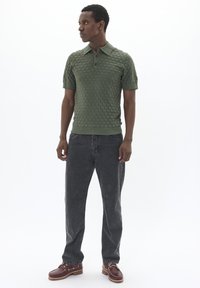 Zöld kötött pólóing, egyszínű kockás mintával, rövid ujjakkal és gallérral, sötétszürke egyenes lábú farmerrel és barna cipővel párosítva.