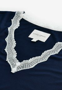 Granatowa bluzka z białą koronką wzdłuż dekoltu, z dwoma białymi guzikami. Metka z napisem "Laura Ashley" oraz "Since 1953."