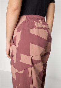 Cargo-byxor i ett geometriskt mönster av mauve och beige, med elastisk midja, sidofickor och sömdetalj som visar varumärket.