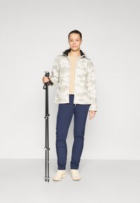 Lett, mønstret jakke i nyanser av grått og hvitt, med svart krage. Kombinert med marineblå slim-fit bukser og lette tursko.