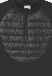 Svart kvartslång zip-tröja med en quiltad stoppad panel på bröstet och slätt tyg på ärmarna och ryggen. Texturerad och stilren.