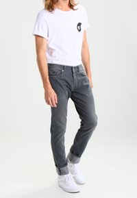Jeans de mezclilla gris con un ajuste slim, con puños enrollados, combinados con una camiseta blanca que presenta un pequeño diseño gráfico negro en el pecho. Zapatillas blancas.