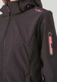 Veste softshell noire avec col haut, dotée de fermetures éclair roses et d'accents assortis. Comprend une poche zippée sur la manche et un détail de logo.