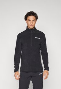 Svart fleece genser med halv-glidelås og lange ermer. Har et TERREX-logo på brystet, glatt tekstur og tettsittende design.
