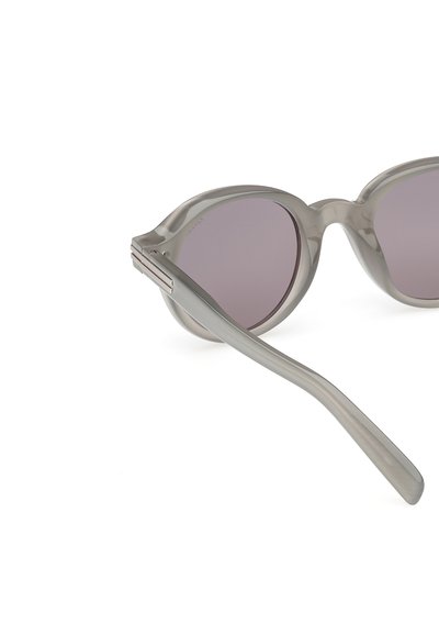 Sluneční brýle s průhledným šedým rámem, kulatými čočkami s mírným gradientním zabarvením a hladkými, zakřivenými nohami s kovovými akcenty.
