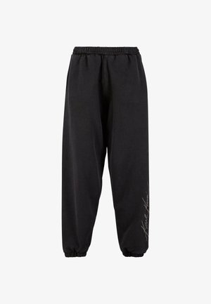 Pantalones de chándal negros hechos de una tela suave con una cintura elástica. Tobillos entallados y detalle de texto impreso en un lado. Corte casual y relajado.