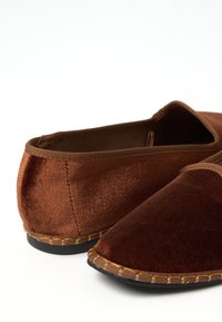 Braune Samt-Hausschuhe mit weicher Textur, spitzes Design und einem kontrastierenden, beige genähten Besatz entlang der Sohle. Keine sichtbaren Beschläge.