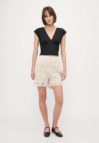 Black fitted V-neck top with short sleeves paired with cream lace shorts featuring floral patterns and scalloped edges. Glossy black flats.