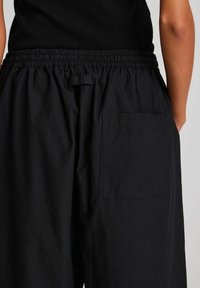 Black, lightweight, elastic-waist pants with a single back pocket, featuring a smooth texture and relaxed fit.