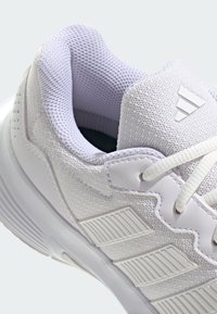 Białe buty sportowe z teksturowaną cholewką, siateczkowym wykończeniem, gumową podeszwą oraz charakterystycznym akcentem w postaci trzech pasków po boku.