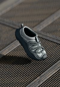 Szare sportowe buty z teksturowaną cholewką, elastycznymi sznurówkami i amortyzującą podeszwą, z uchwytem na pięcie.