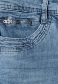 Jean en denim bleu avec un lavage clair, doté d'une poche zippée et de coutures le long de la taille et des bords de poche.