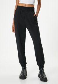 Zwarte joggingsbroek met een smocktailleband, zijzakken en elastische boorden, gemaakt van een zachte stof die geschikt is voor casual gebruik.