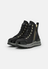 Sneaker alte nere con accessori dorati, chiusura con lacci sul davanti, zip laterale, suola elevata e testo stampato lungo il lato. Materiali morbidi e testurizzati.