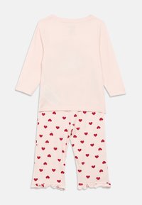 Svijetloružičasta majica dugih rukava u kombinaciji s odgovarajućim hlačama s uzorkom crvenih srca i naboranim rubovima.