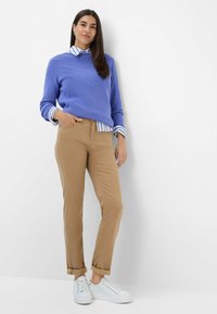 Un pull côtelé bleu clair superposé sur une chemise rayée blanche et bleue. Un pantalon chino beige et des baskets blanches complètent l'ensemble. Un design décontracté et ajusté.