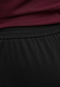 Mustien housujen joustava vyötärönauha, yhdistettynä sisään puserrettuun viininpunaiseen yläosaan, jossa näkyy kangasrakenne ja ompeleiden yksityiskohdat.