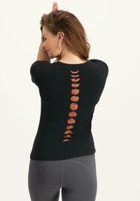 Mustaharju musta t-paita, jossa on teksturoitu oranssi kuu vaihe -painatus, joka kulkee pystysuoraan selän keskellä.